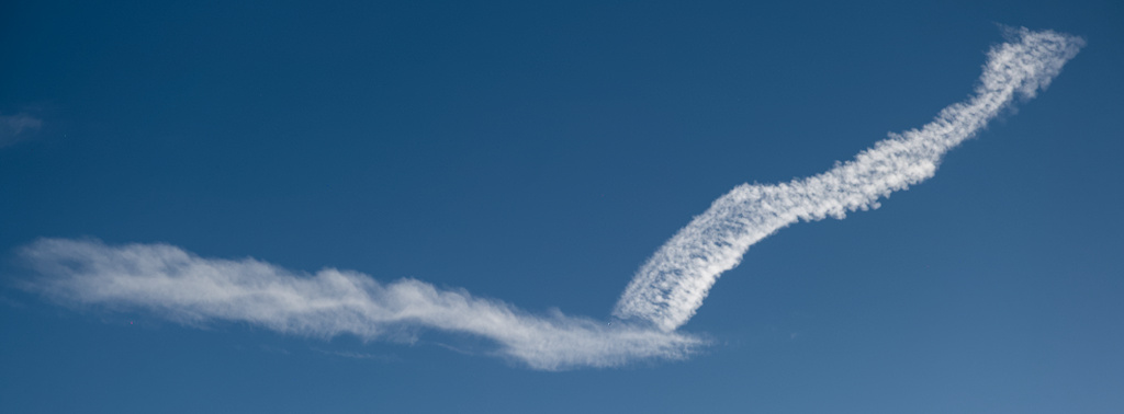A photograph of white clouds, possibly contrails, against a blue sky, forming a obtuse V shape.